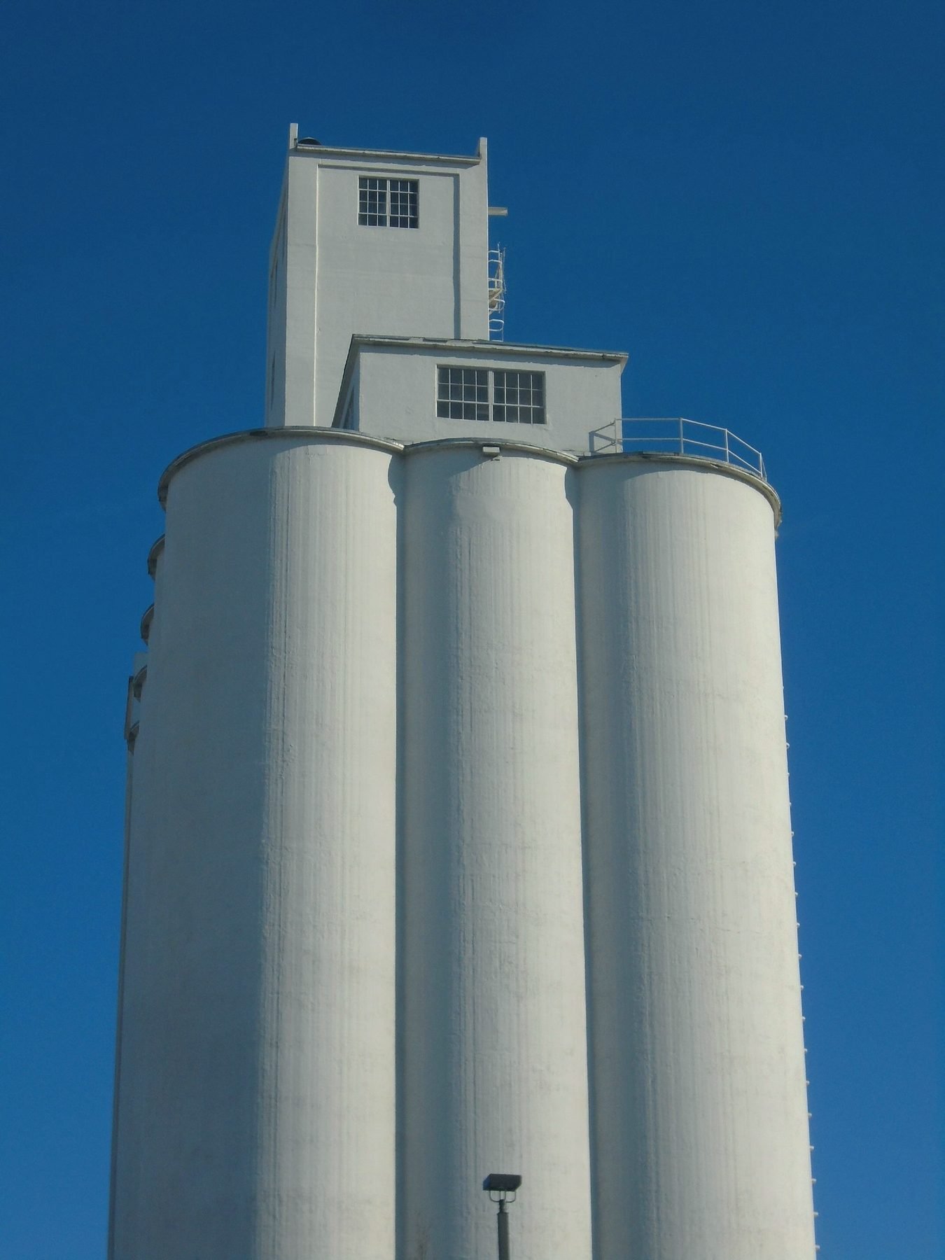 A white concrete grain elevator and headhouse against a deep blue sky